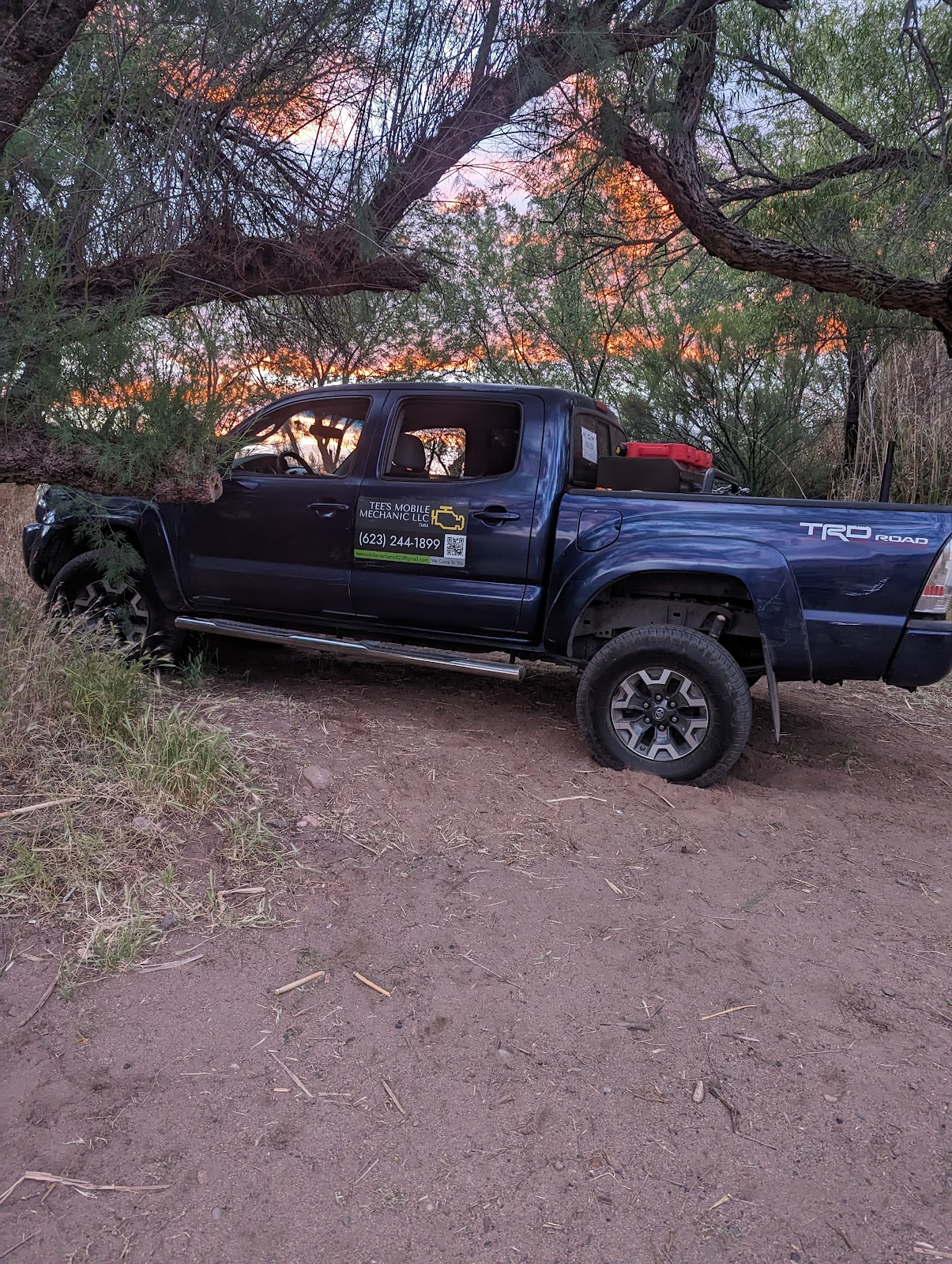 Tee's navy Toyota Tacoma TRD parked under mesquite trees at desert sunset, with the Tee's Mobile Mechanic magnet on the door